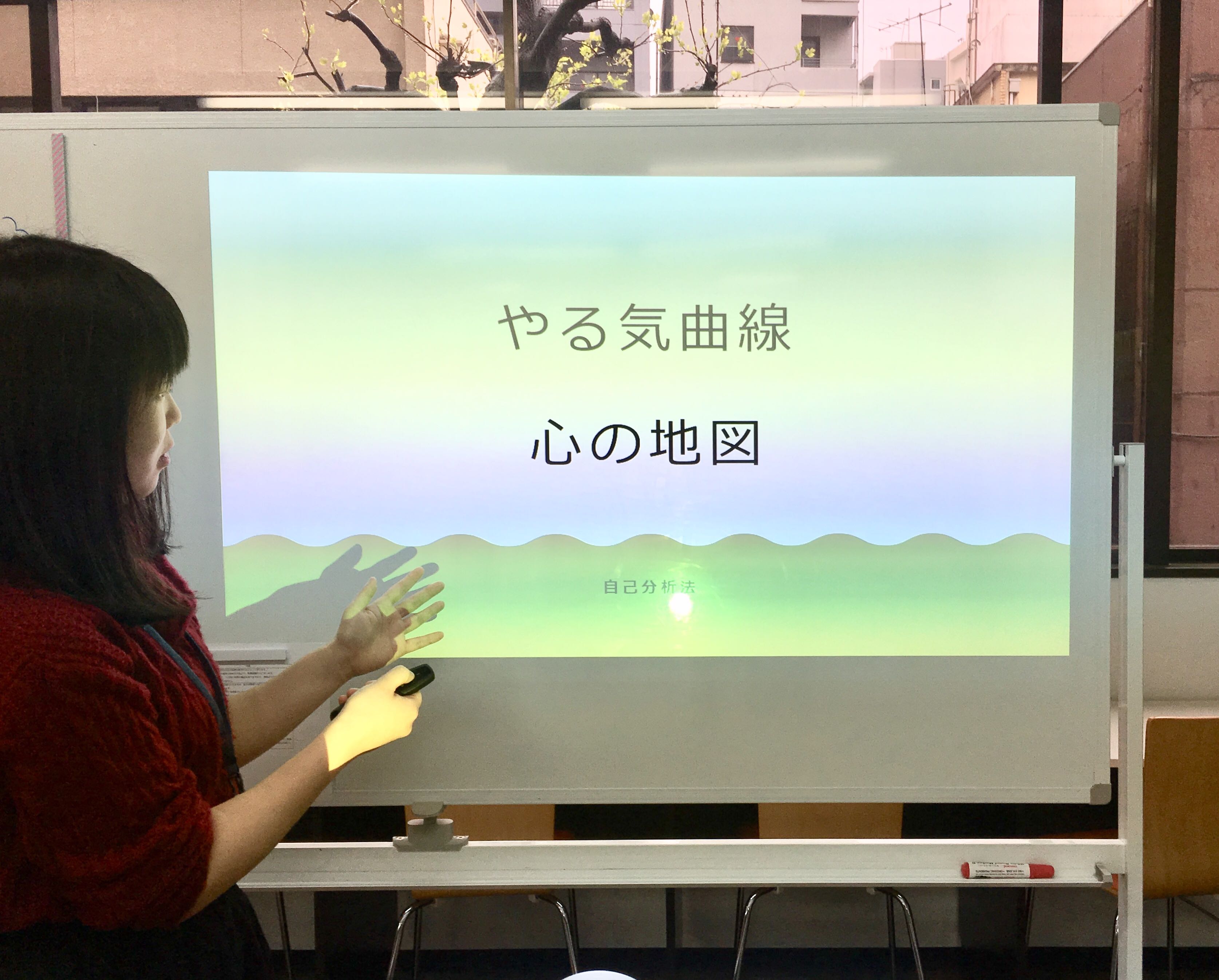 「やる気曲線プログラム」内で、モチベーションについて学ぶスライドを基に説明を行う女性スタッフ