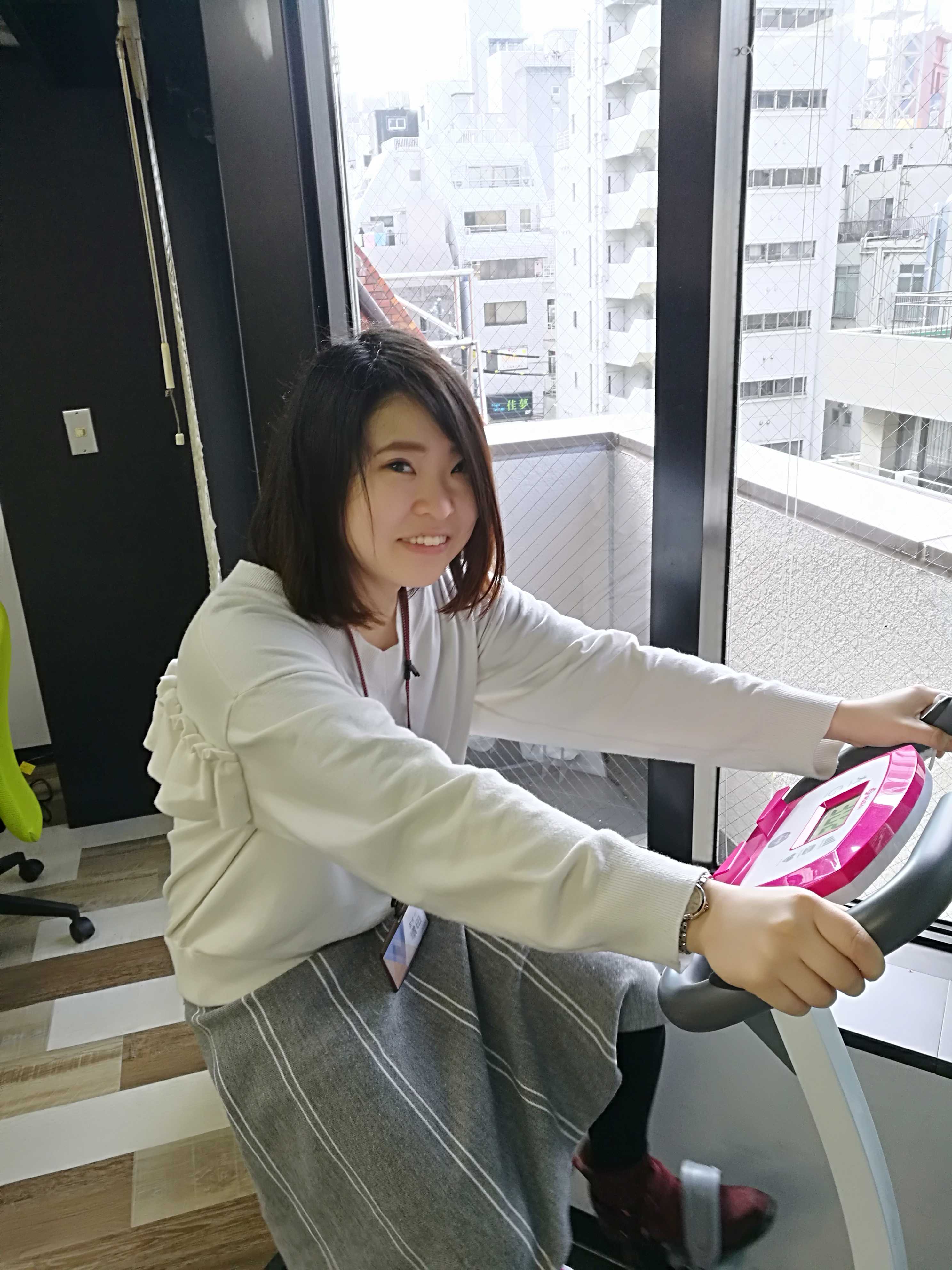 窓際に設置されたバイクマシンに跨る女性スタッフ